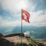 Flag of Switzerland on a hill with a view of mountains
